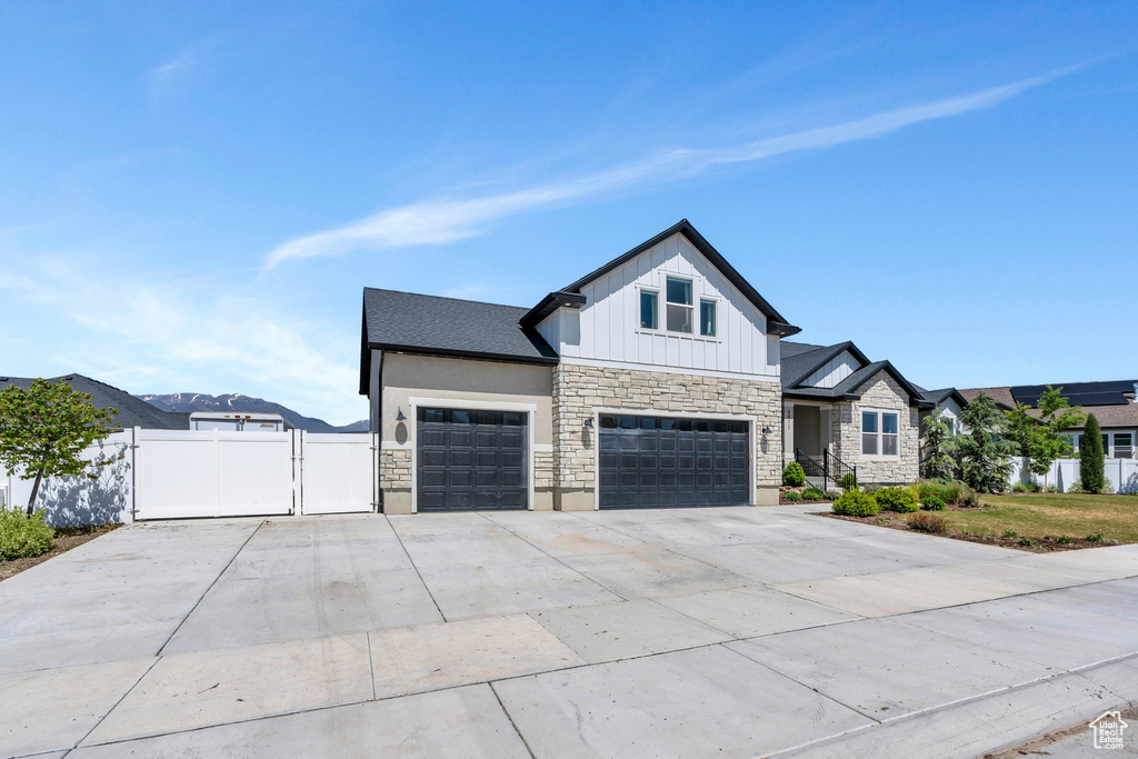 Modern farmhouse featuring stone siding, a gate, concrete driveway, board and batten siding, and an attached garage