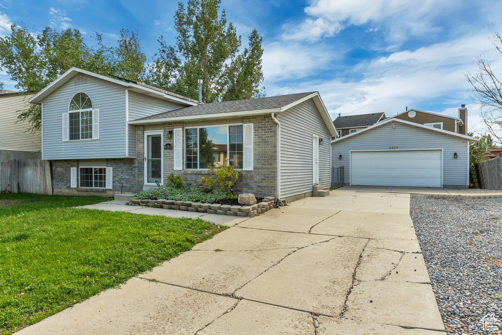 Tri-level home featuring a garage, an outdoor structure, and brick siding