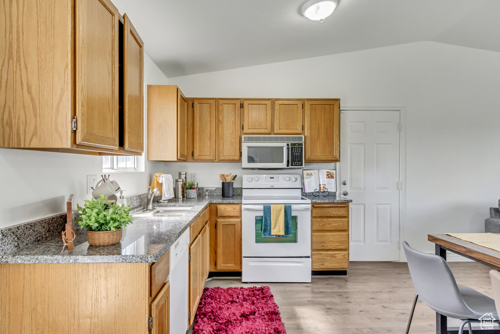 Kitchen with white appliances, a sink, lofted ceiling, light wood-type flooring, and stone counters