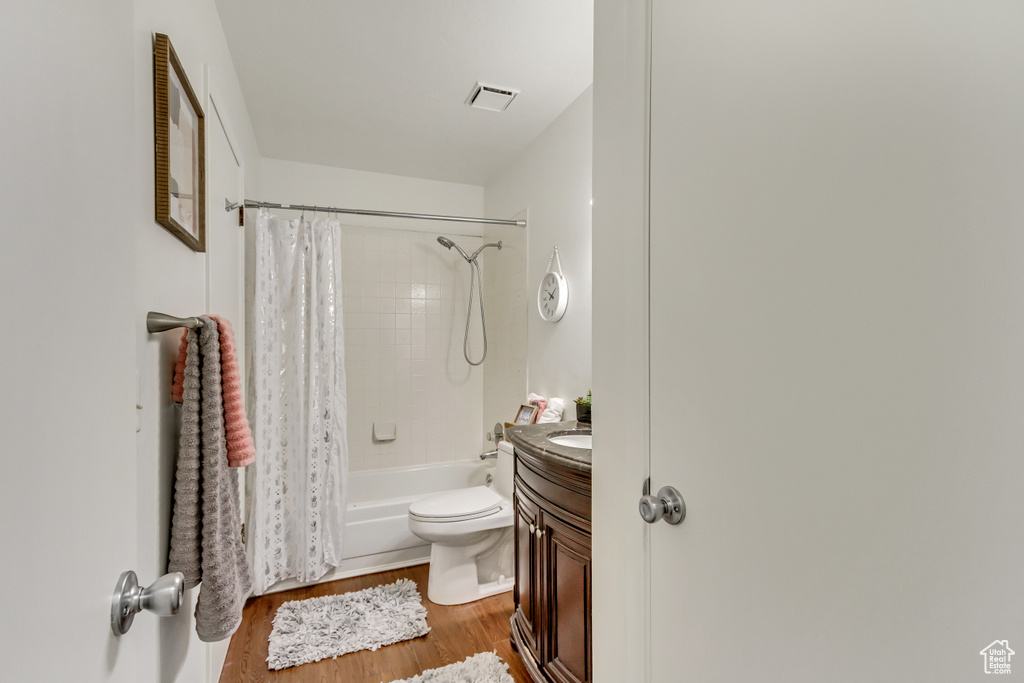 Bathroom featuring wood finished floors, vanity, shower / bathtub combination with curtain, and toilet