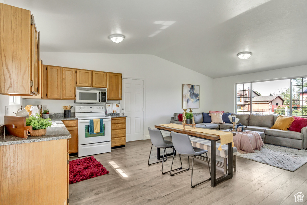 Kitchen featuring stainless steel microwave, electric range, vaulted ceiling, light wood finished floors, and open floor plan