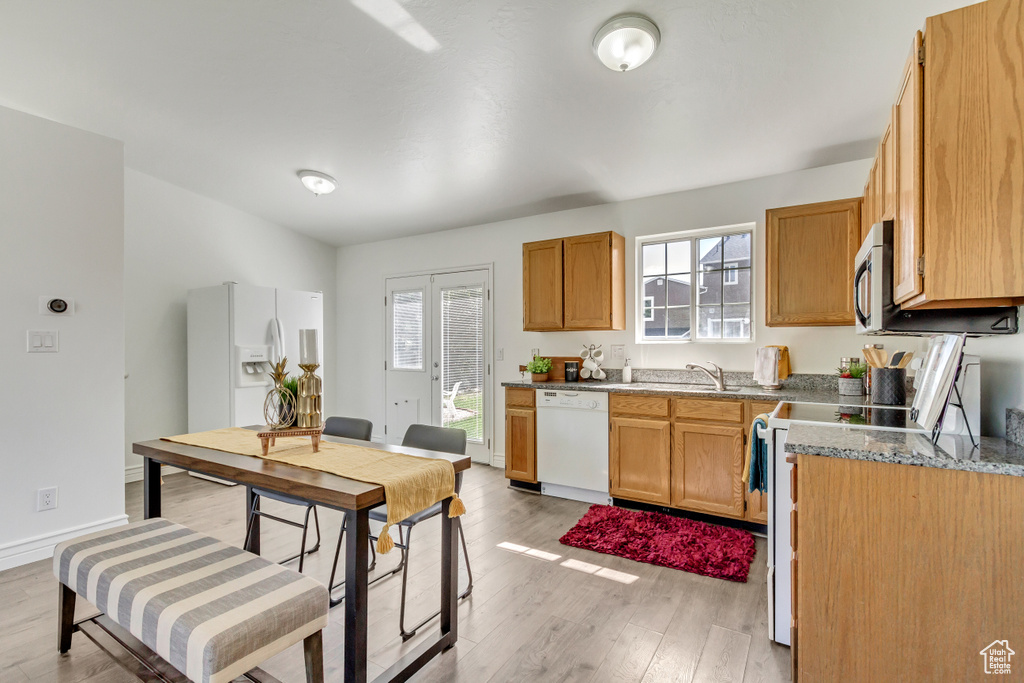 Kitchen featuring white appliances, light wood-type flooring, stone counters, a sink, and baseboards