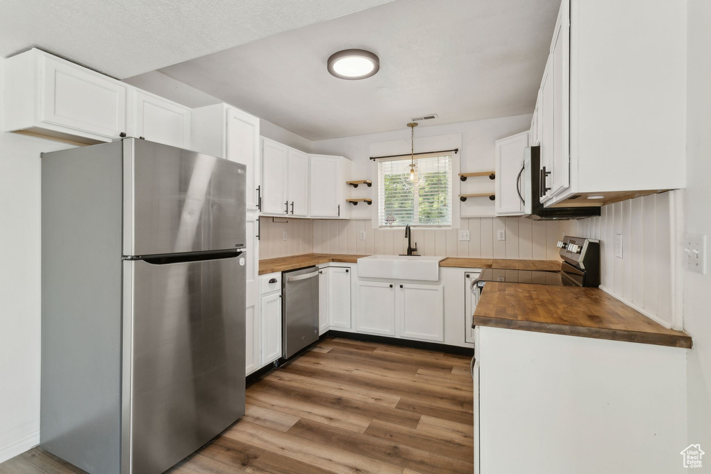 Kitchen with appliances with stainless steel finishes, butcher block countertops, open shelves, and a sink