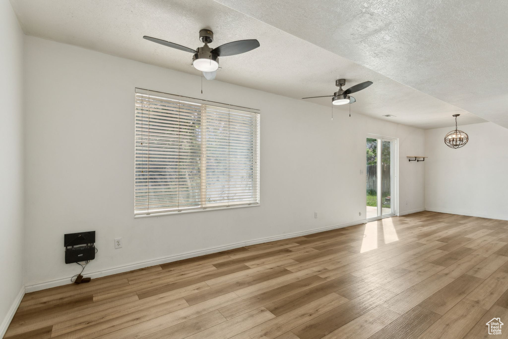 Empty room featuring ceiling fan, light wood-style flooring, a chandelier, a textured ceiling, and baseboards