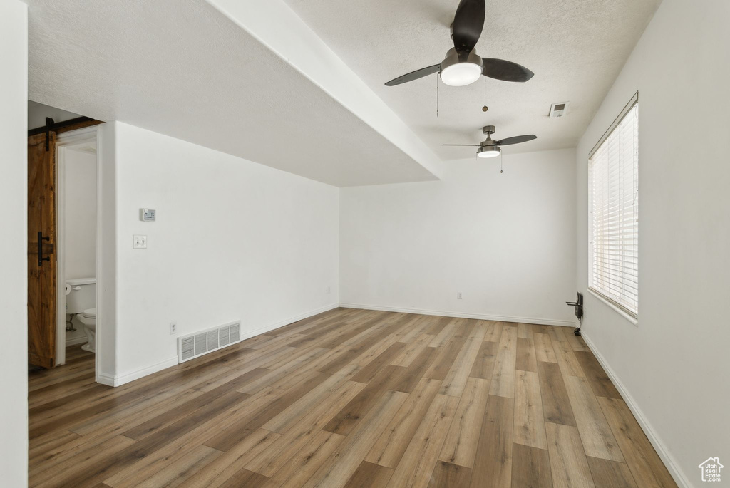 Additional living space featuring light wood-style flooring, a ceiling fan, a barn door, and baseboards