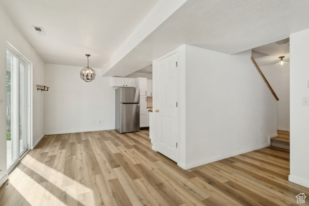 Unfurnished dining area with light wood-type flooring, a chandelier, and baseboards