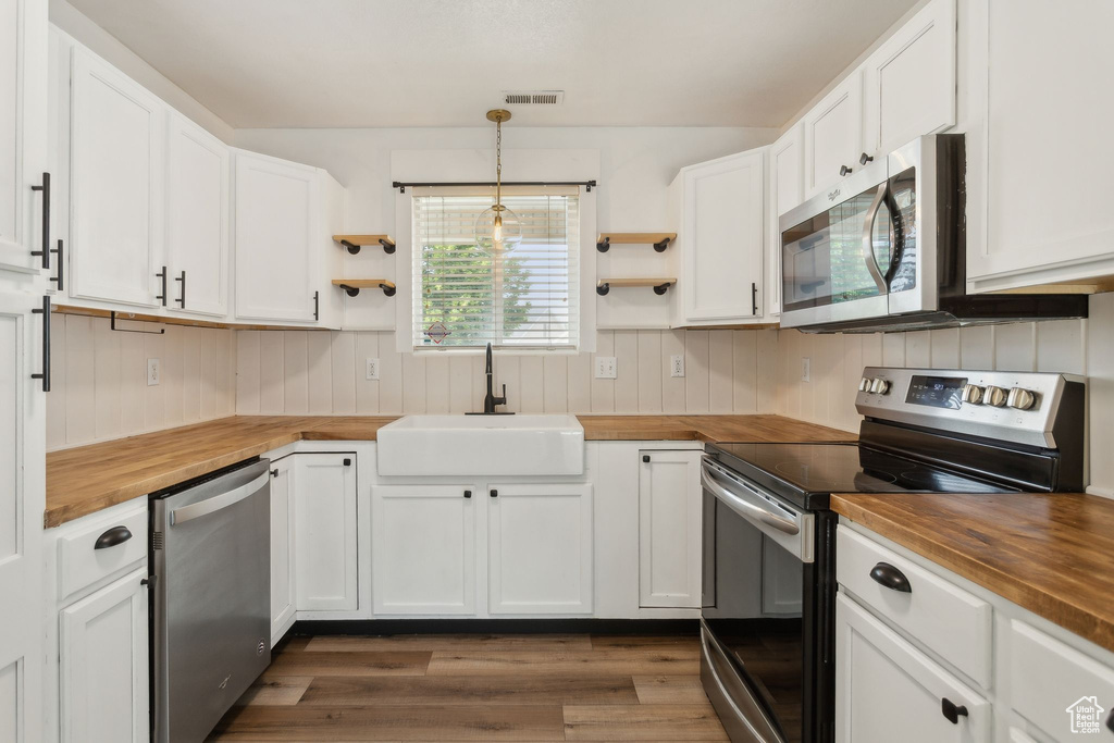 Kitchen with butcher block counters, stainless steel appliances, a sink, open shelves, and wooden walls