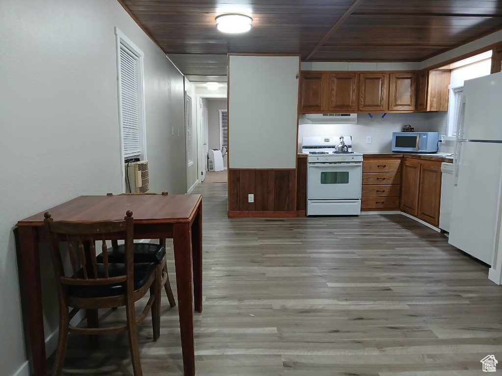 Kitchen with white appliances, wood ceiling, light wood finished floors, under cabinet range hood, and brown cabinetry