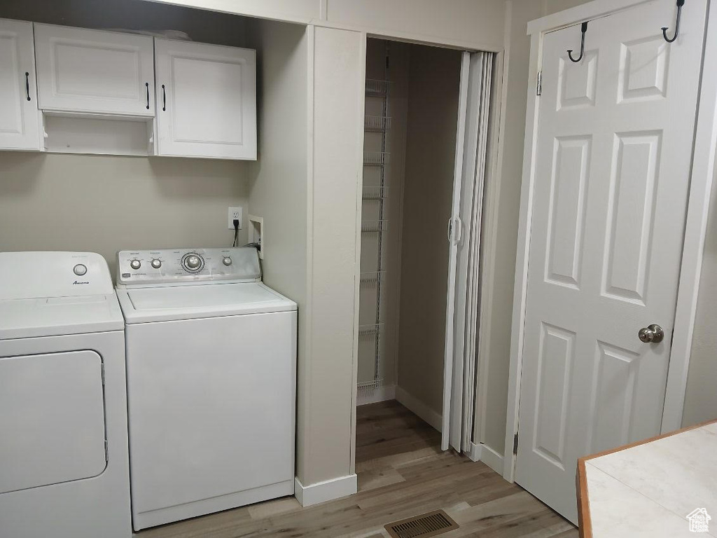 Laundry room with washer and dryer, light wood-style flooring, cabinet space, and baseboards