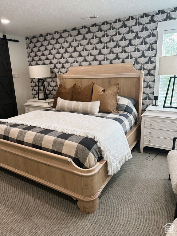 Carpeted bedroom featuring a barn door and a textured ceiling