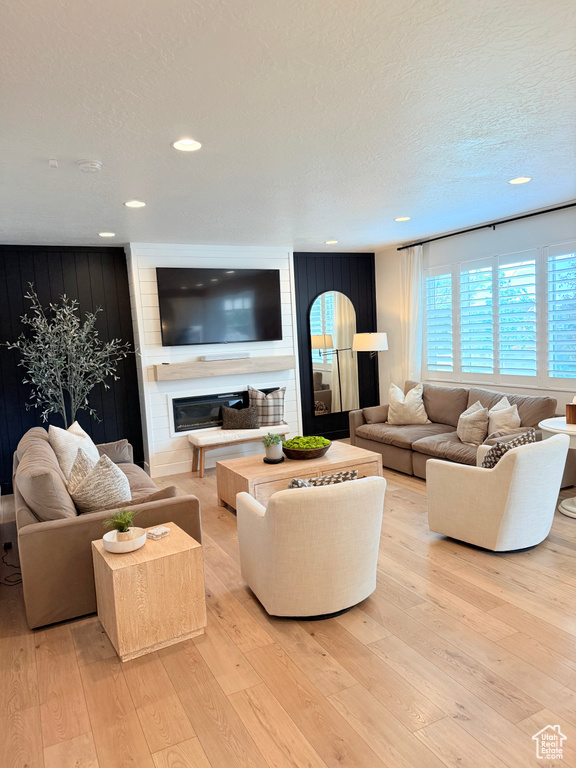 Living room featuring a glass covered fireplace, light wood-style floors, a textured ceiling, and recessed lighting