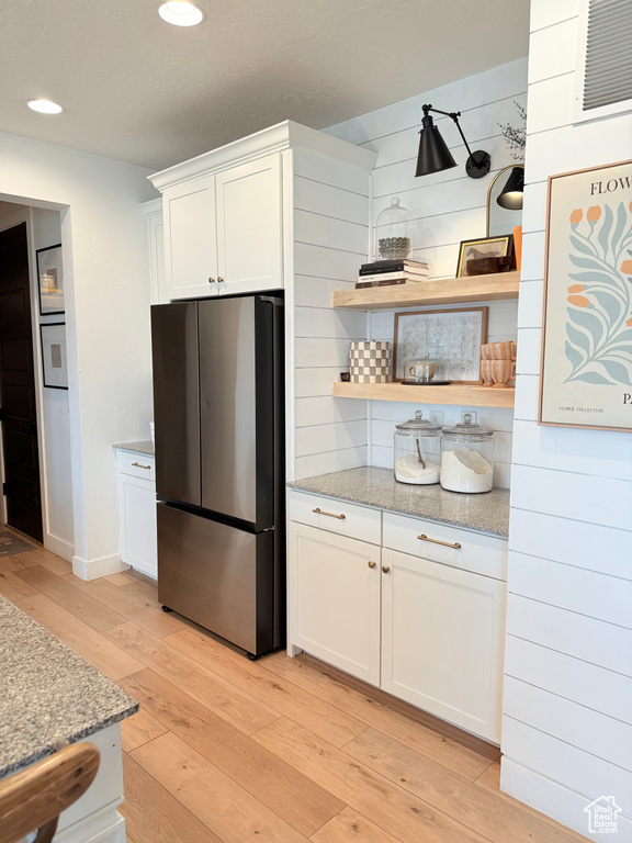 Kitchen featuring freestanding refrigerator, light wood finished floors, white cabinetry, recessed lighting, and light stone countertops