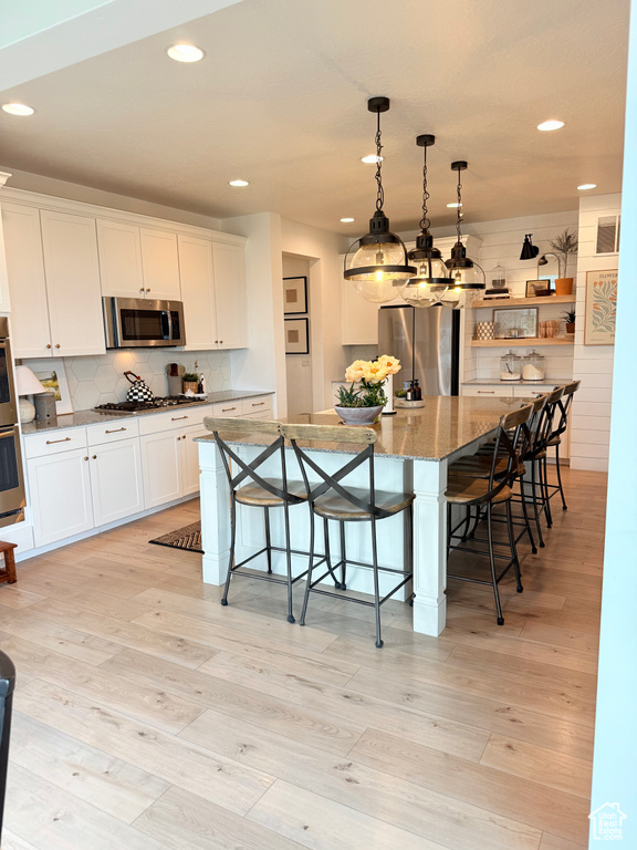 Kitchen featuring appliances with stainless steel finishes, recessed lighting, a kitchen breakfast bar, tasteful backsplash, and white cabinetry