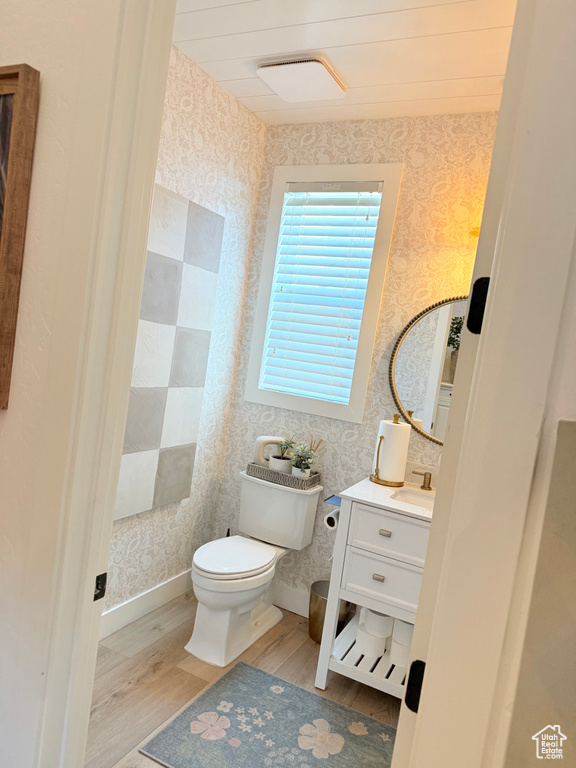Half bathroom featuring wallpapered walls, wood finished floors, vanity, and toilet