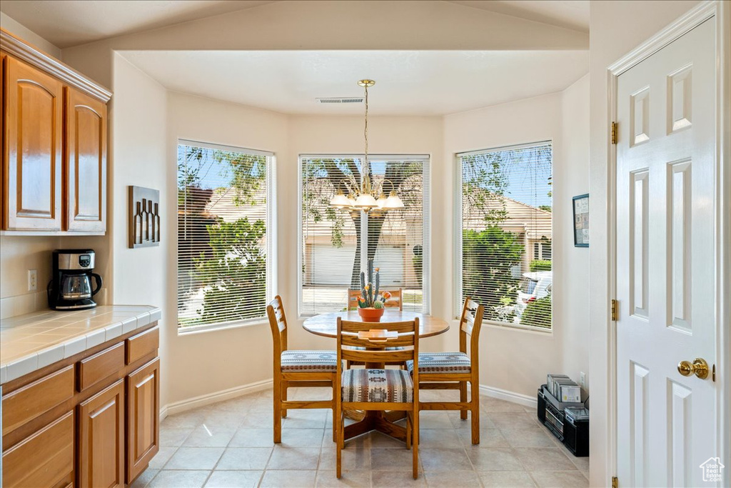 Dining space with a chandelier, baseboards, light tile patterned floors, and vaulted ceiling