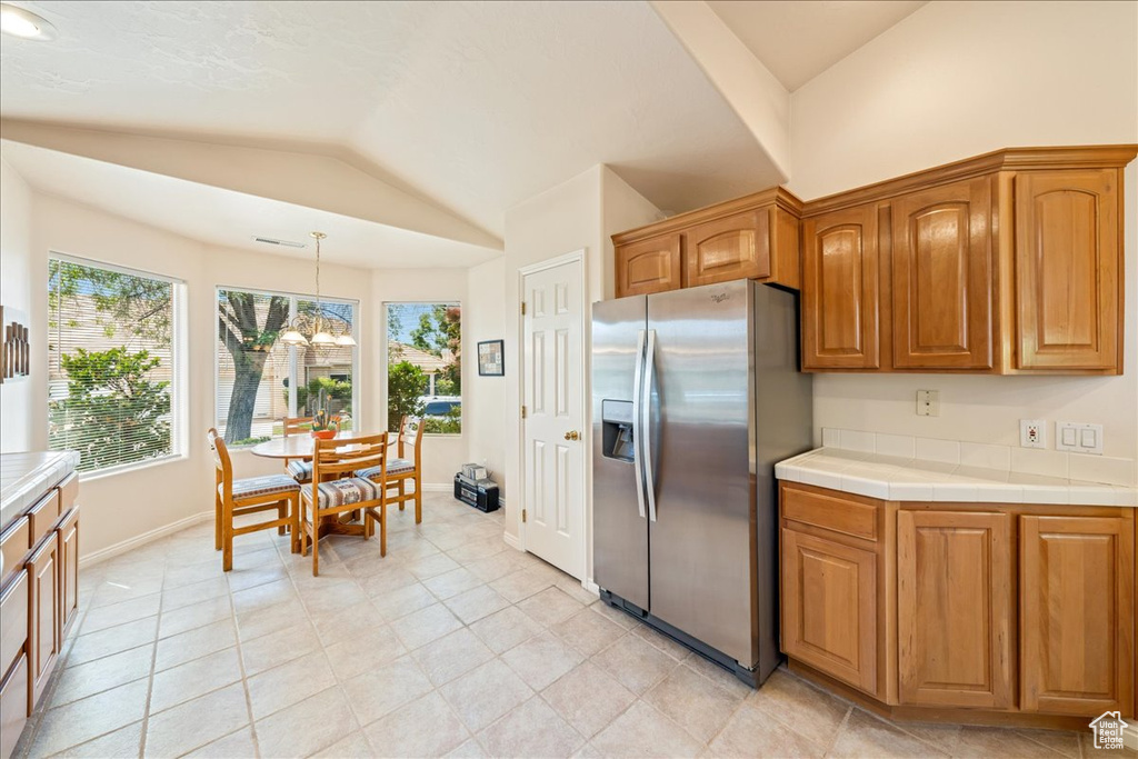 Kitchen featuring stainless steel refrigerator with ice dispenser, lofted ceiling, baseboards, brown cabinets, and a chandelier
