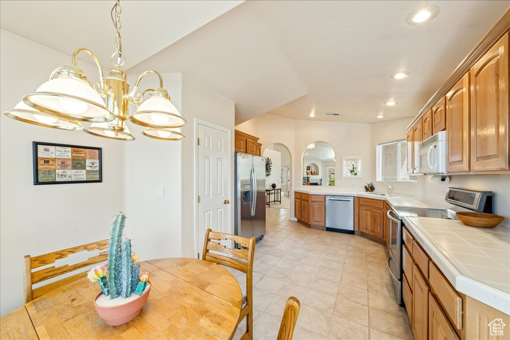 Kitchen with stainless steel appliances, arched walkways, tile countertops, recessed lighting, and a chandelier