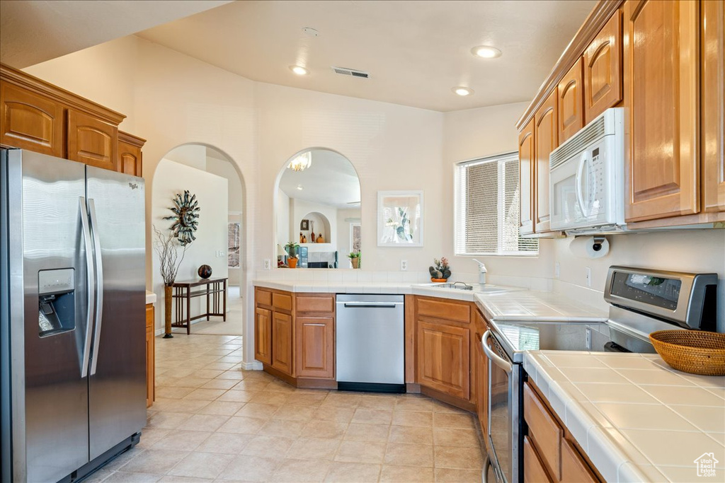 Kitchen featuring appliances with stainless steel finishes, a sink, tile counters, brown cabinets, and recessed lighting