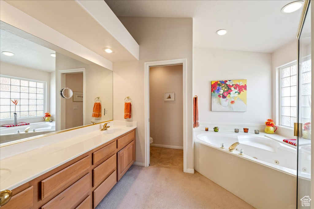 Full bathroom with healthy amount of natural light, double vanity, a bath, toilet, and recessed lighting