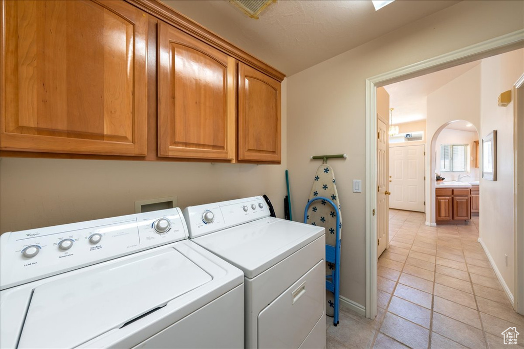 Washroom featuring cabinet space, washing machine and clothes dryer, baseboards, light tile patterned flooring, and arched walkways