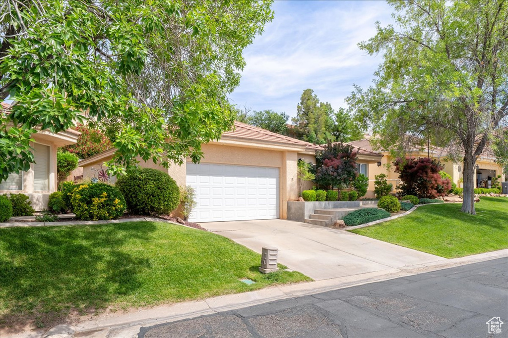 View of property hidden behind natural elements with an attached garage, stucco siding, concrete driveway, a front yard, and a tile roof