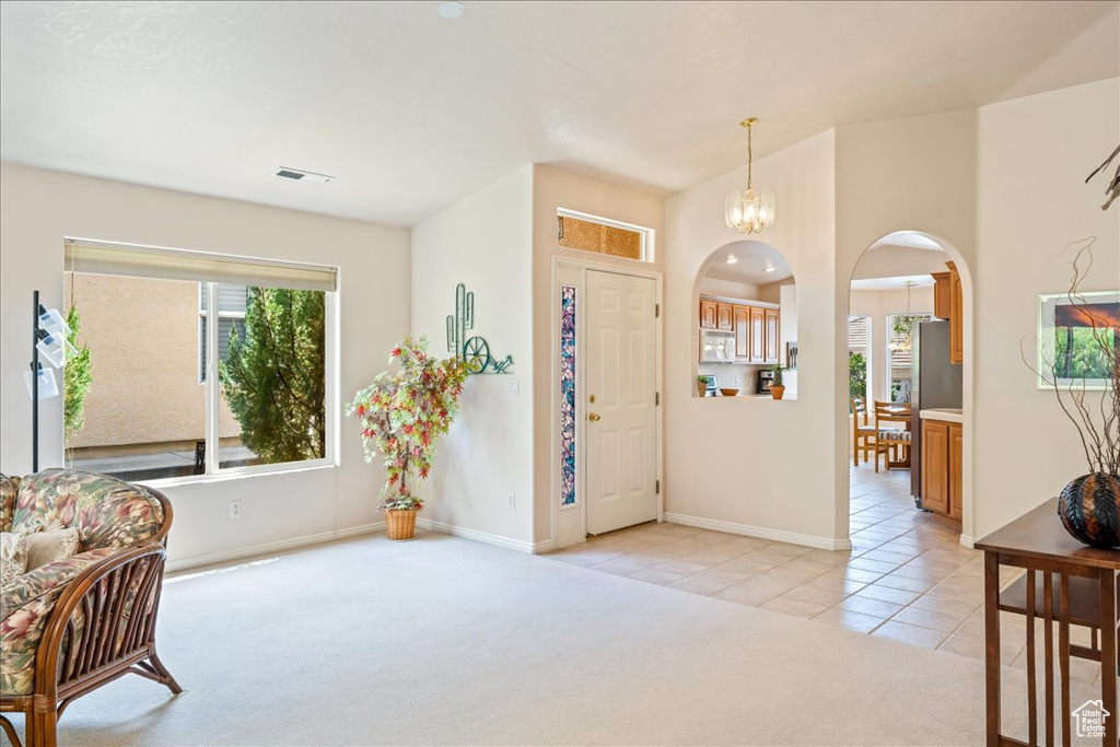Entryway with arched walkways, light tile patterned floors, light colored carpet, baseboards, and a chandelier