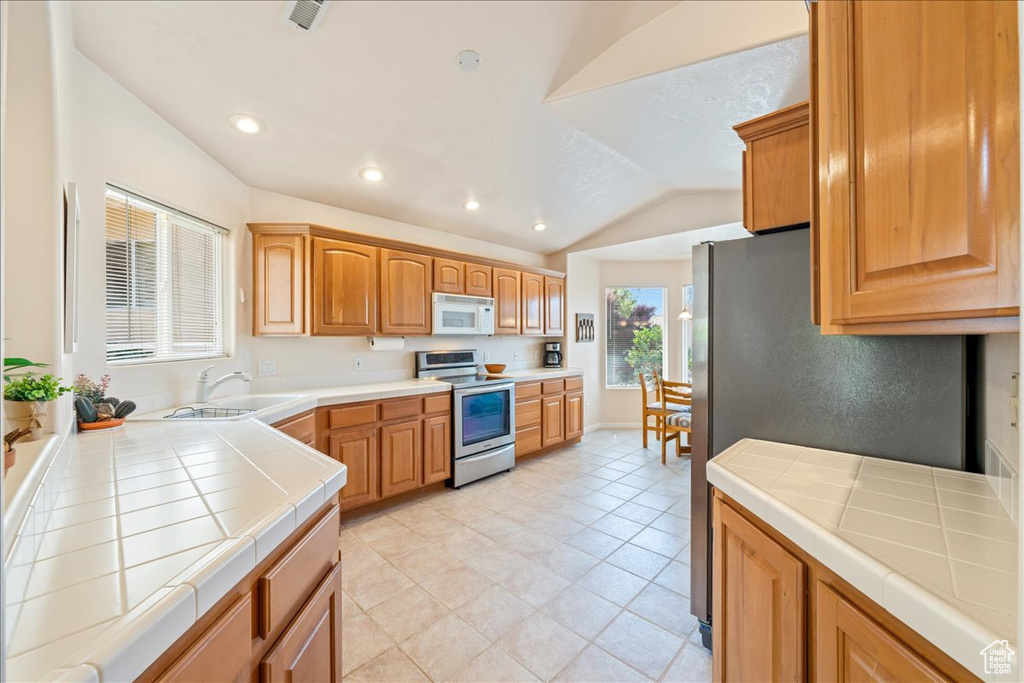 Kitchen featuring stainless steel range with electric cooktop, white microwave, tile counters, a sink, and vaulted ceiling