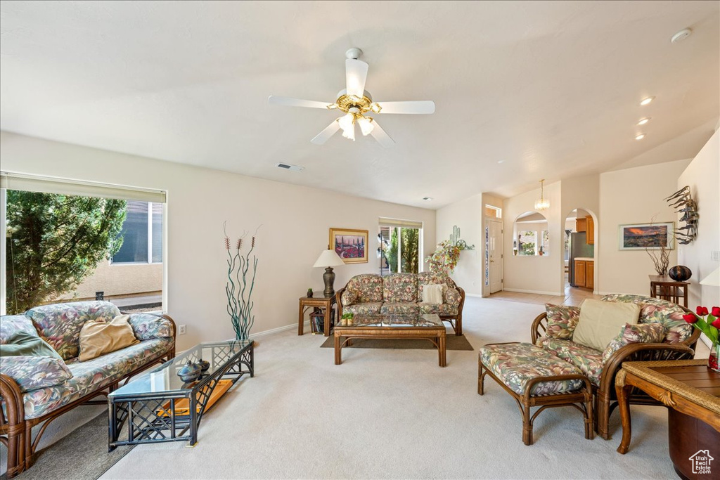 Living room with arched walkways, light carpet, a ceiling fan, vaulted ceiling, and baseboards