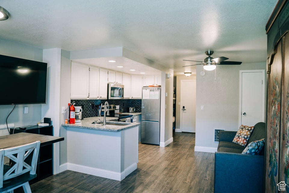Kitchen with appliances with stainless steel finishes, decorative backsplash, a peninsula, dark wood finished floors, and a textured ceiling