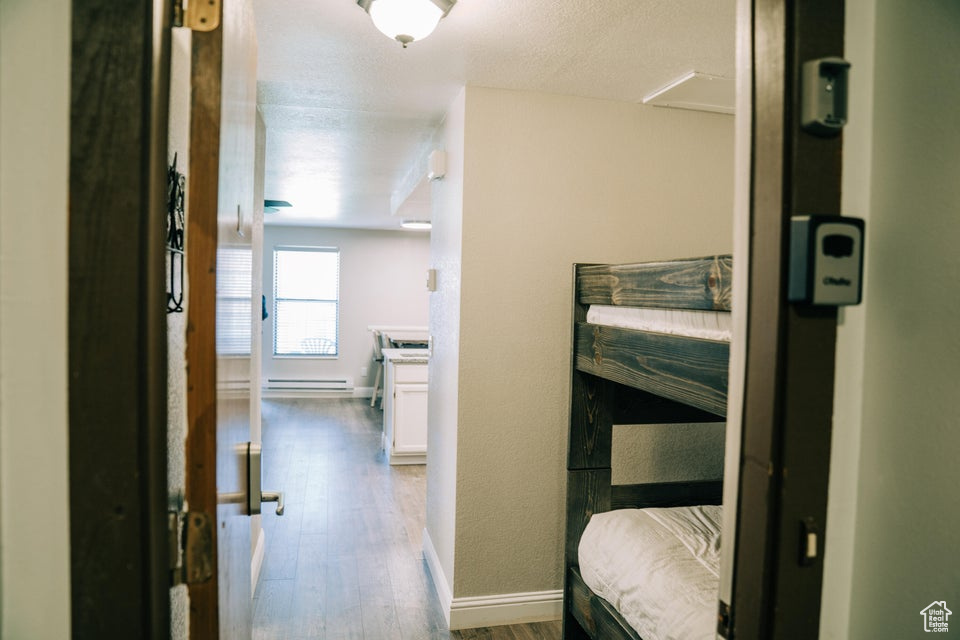 Hallway featuring wood finished floors, a baseboard heating unit, and baseboards