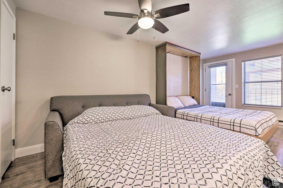 Bedroom with dark wood-style floors, baseboards, ceiling fan, and access to exterior