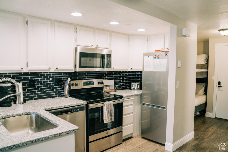 Kitchen with appliances with stainless steel finishes, a sink, light wood-type flooring, white cabinetry, and recessed lighting