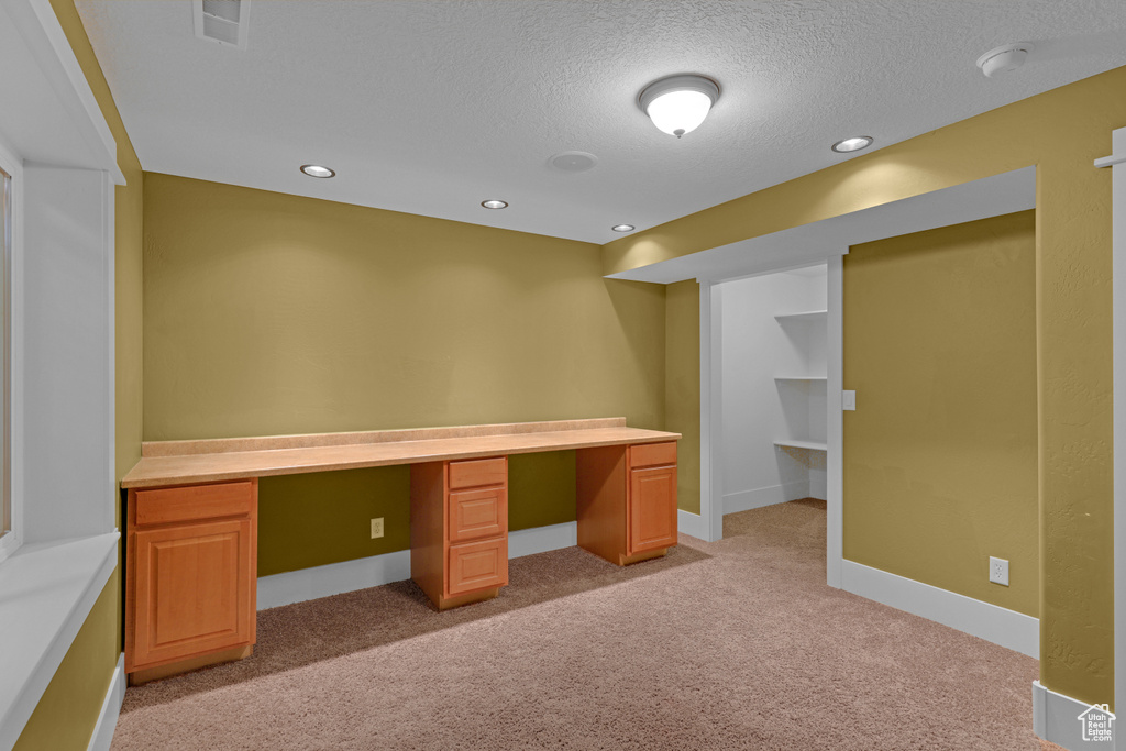 Unfurnished office featuring built in study area, light carpet, a textured ceiling, and recessed lighting