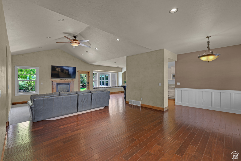 Unfurnished living room featuring wood finished floors, ceiling fan, lofted ceiling, wainscoting, and a glass covered fireplace