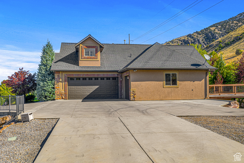 View of front of home featuring driveway, a shingled roof, stucco siding, a garage, and a mountain view