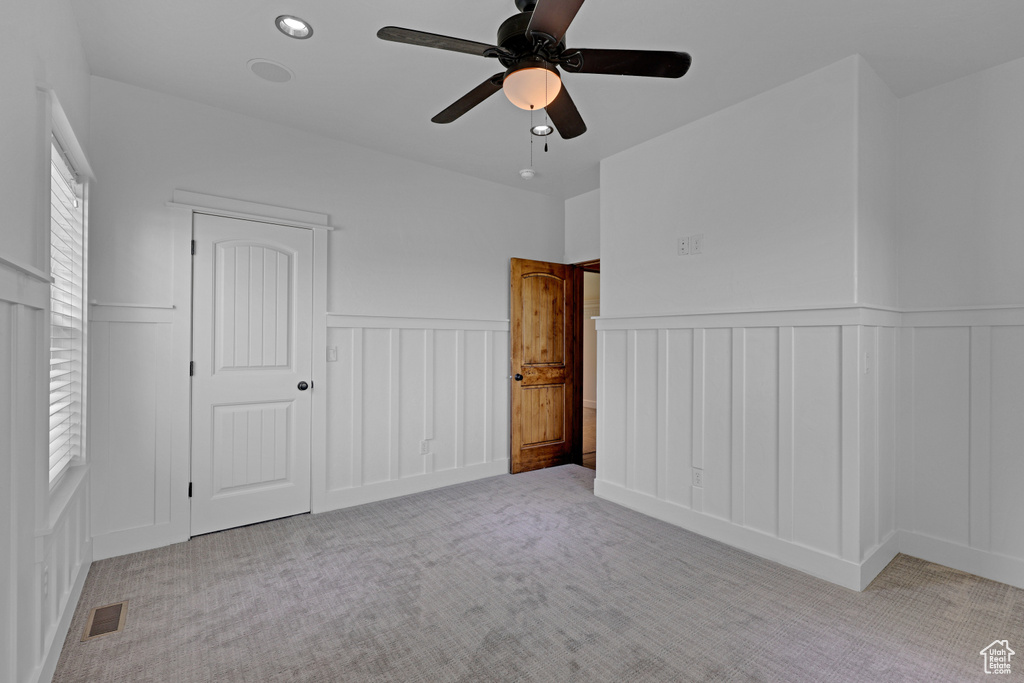 Unfurnished bedroom featuring a decorative wall, carpet floors, wainscoting, and ceiling fan