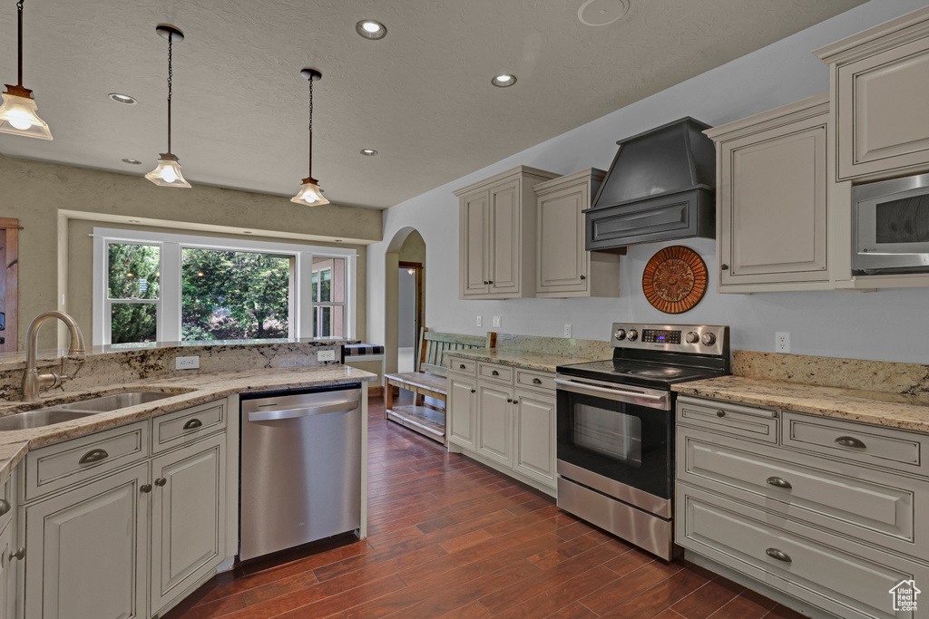 Kitchen with appliances with stainless steel finishes, custom exhaust hood, a sink, arched walkways, and dark wood-style flooring