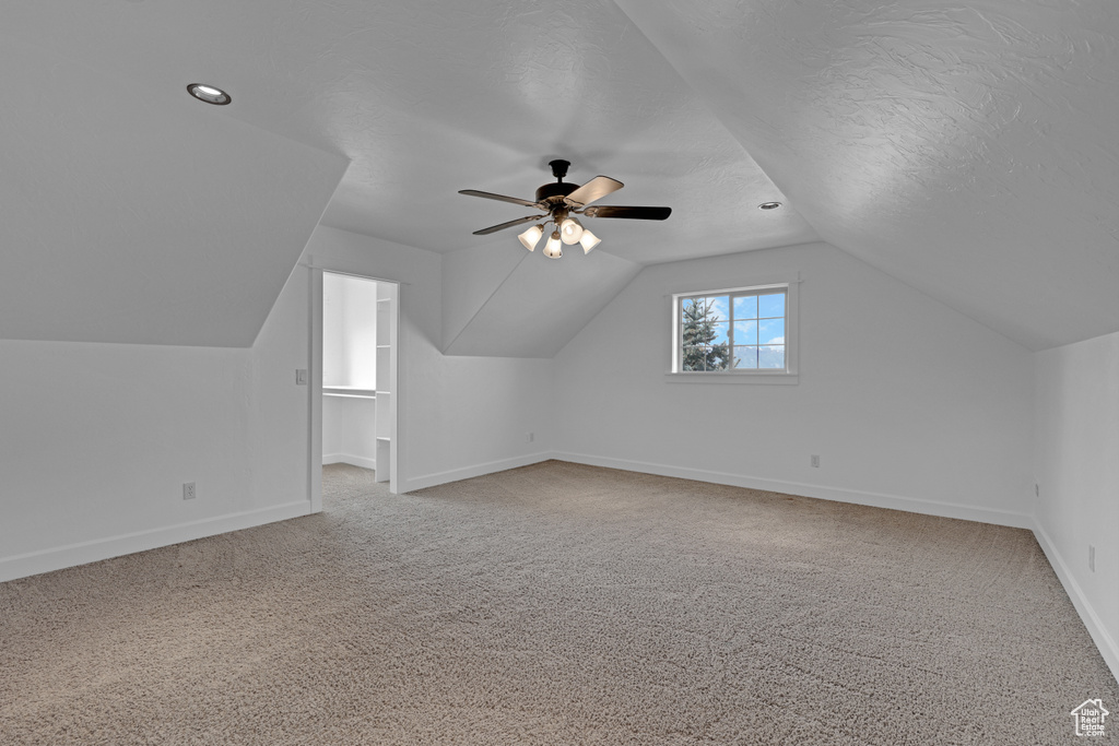 Additional living space with baseboards, light carpet, vaulted ceiling, ceiling fan, and a textured ceiling