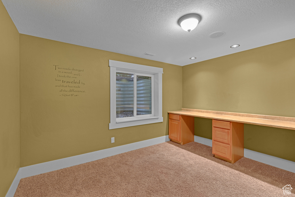 Unfurnished office with built in desk, light carpet, a textured ceiling, baseboards, and recessed lighting