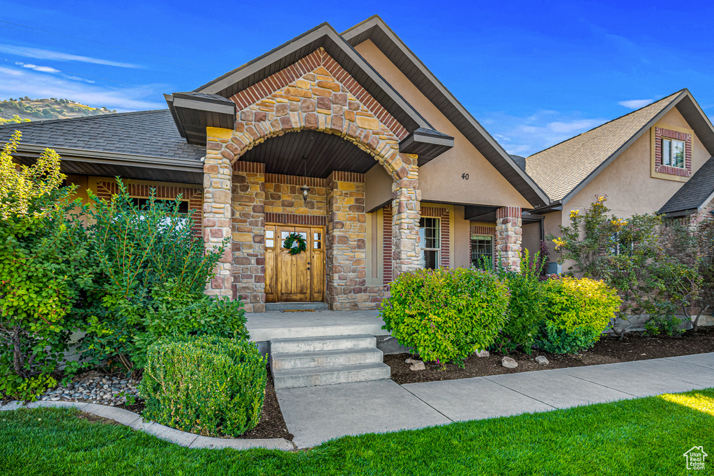 Doorway to property featuring stone siding, stucco siding, and roof with shingles