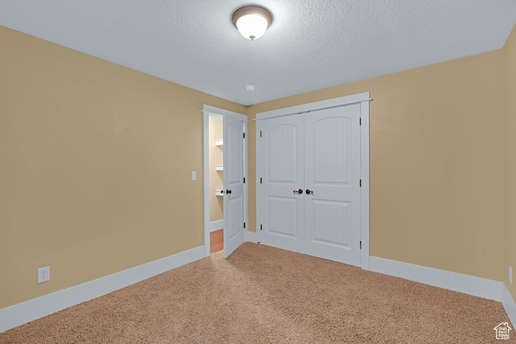 Unfurnished bedroom with carpet floors, a textured ceiling, a closet, and baseboards