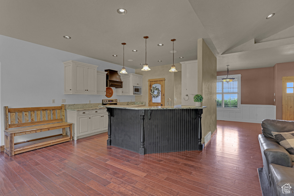 Kitchen with stainless steel microwave, custom range hood, wood finished floors, a wainscoted wall, and light stone countertops
