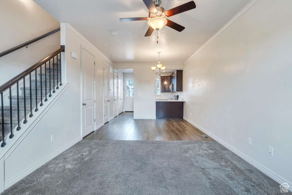 Unfurnished living room with dark carpet, a chandelier, ornamental molding, a ceiling fan, and baseboards