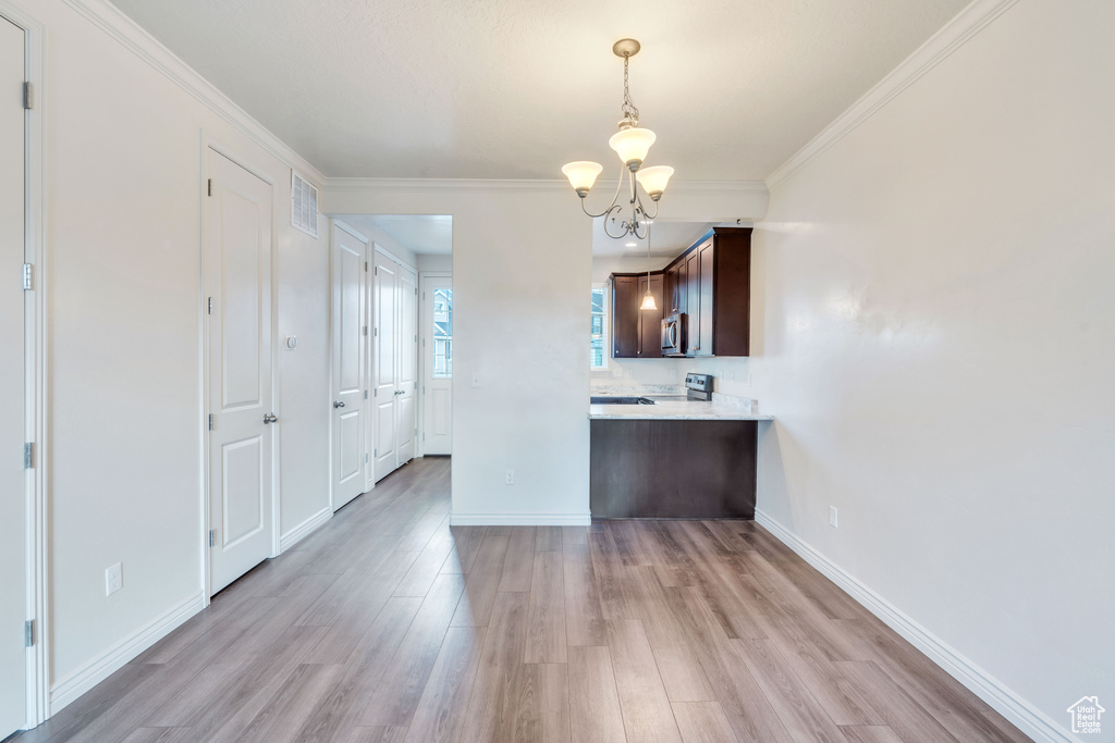 Kitchen featuring a chandelier, light countertops, dark brown cabinetry, light wood finished floors, and pendant lighting