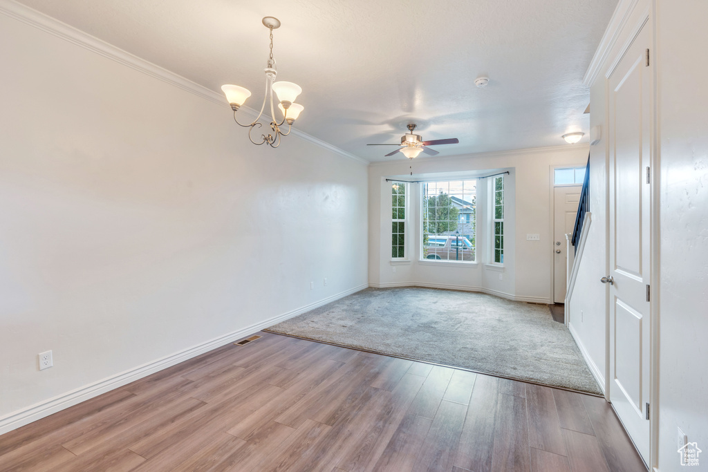 Empty room featuring crown molding, light wood-type flooring, a chandelier, baseboards, and ceiling fan