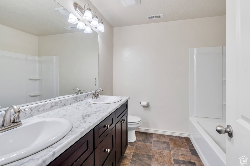 Bathroom featuring double vanity, stone finish flooring, baseboards, and toilet