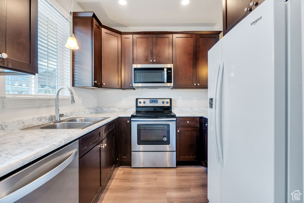 Kitchen with appliances with stainless steel finishes, a sink, light wood-style floors, dark brown cabinets, and recessed lighting