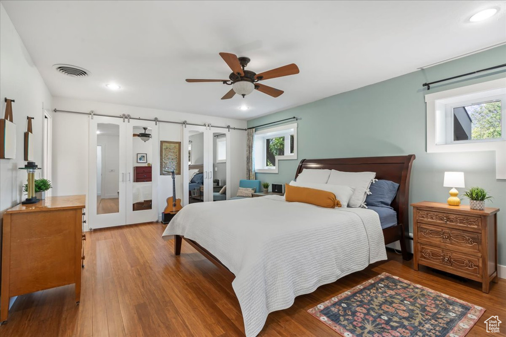 Bedroom with multiple windows, wood finished floors, a barn door, recessed lighting, and ceiling fan