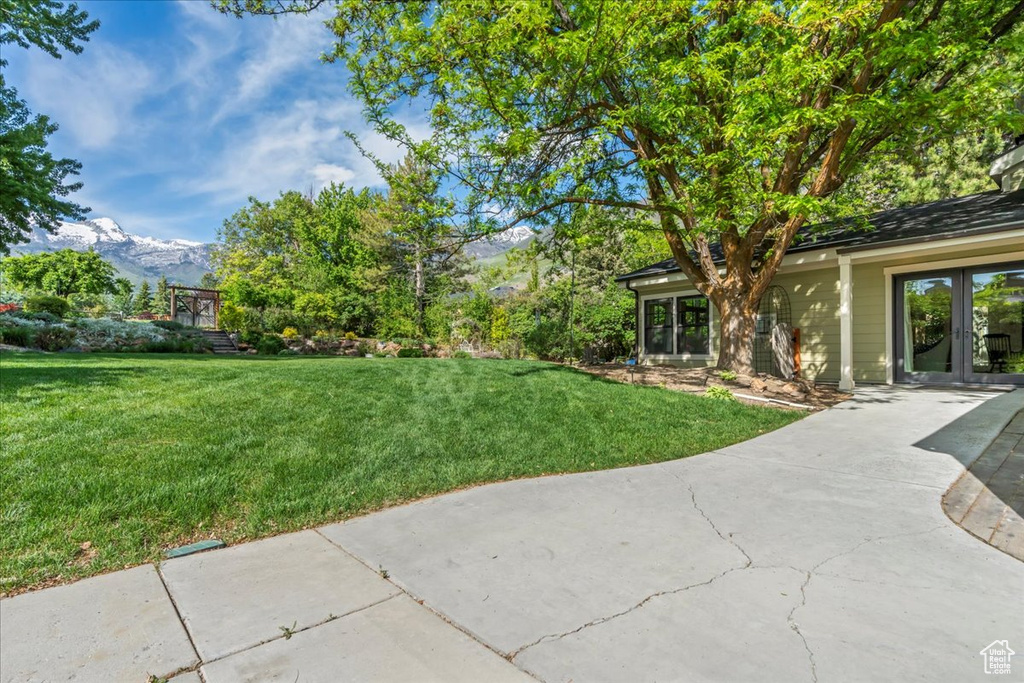 View of grassy yard with french doors, a mountain view, and driveway
