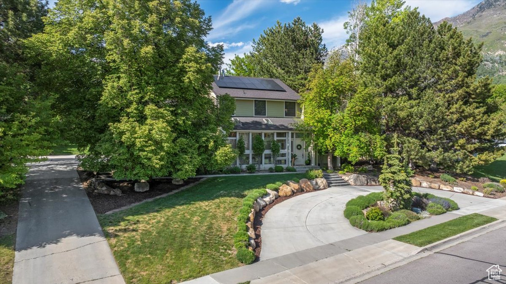 Obstructed view of property featuring curved driveway, a front lawn, and roof mounted solar panels